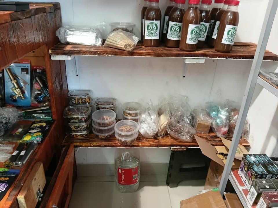 Bottles of Bobo's Cana Cartel Roots Tonic above containers of baked goods on a shop shelf